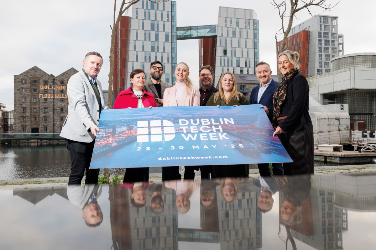 Five people standing in front of the water in Spencer Dock. THey are holding a branded sign launching Dublin Tech Week. The Bolands Mill and Google EU HQ are in the background.